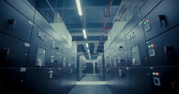 A view of a hallway in a data center filled with server racks and control panels.