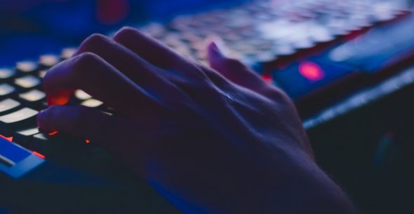 A close-up of a hand resting on a computer keyboard with illuminated keys and a dark background.