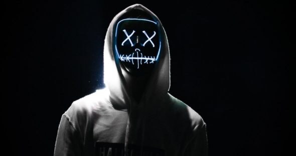 A silhouetted figure wearing a hooded sweatshirt with a glowing mask featuring a face with X's for eyes and a stitched mouth.