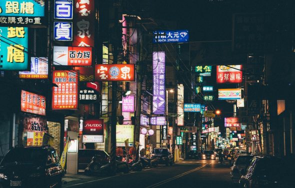 A bustling street at night filled with colorful neon signs and illuminated storefronts.