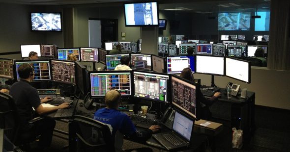 A control room featuring multiple workstations with large screens displaying data,graphs,and monitors.