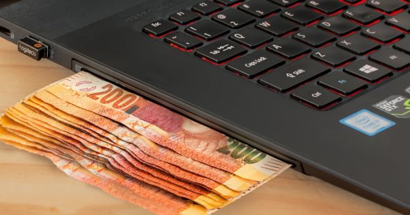 A stack of banknotes partially inserted into a laptop's USB port,illustrating a humorous concept of money and technology.