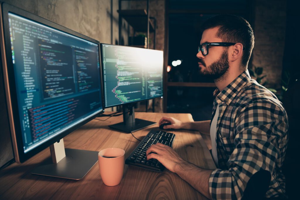 A person working at a desk with dual monitors displaying code