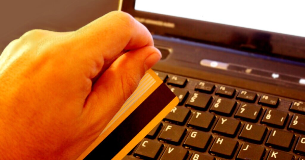 A hand holding a credit card above the keyboard of a laptop.