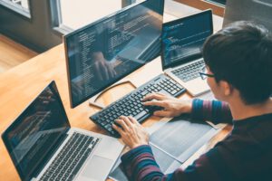 A person working on coding tasks using multiple monitors and laptops