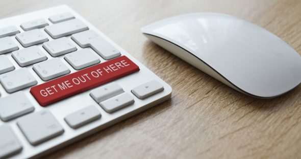 A keyboard featuring a red button labeled 'GET ME OUT OF HERE' next to a white computer mouse on a wooden surface.