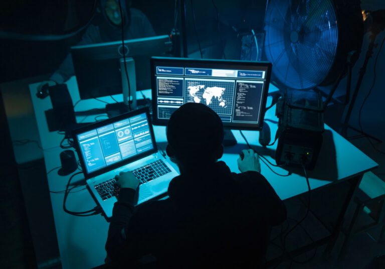 A person working at a computer workstation with multiple screens in a dimly lit room.