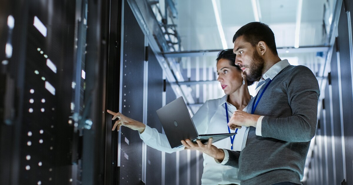 Two professionals collaborating in a data center,examining data on a laptop while interacting with server infrastructure.