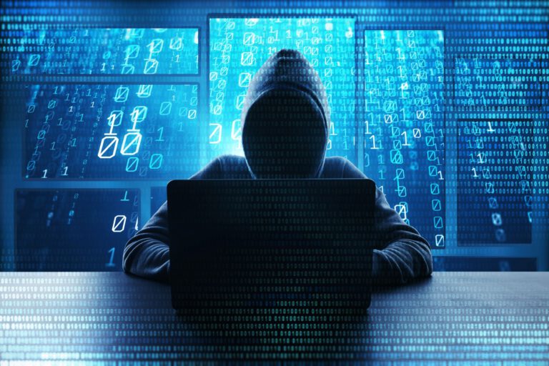 Silhouette of a hacker in a hoodie working on a laptop with binary code.