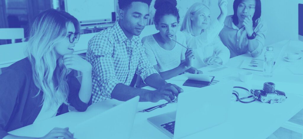 A group of five people engaged in a discussion around a laptop during a meeting.