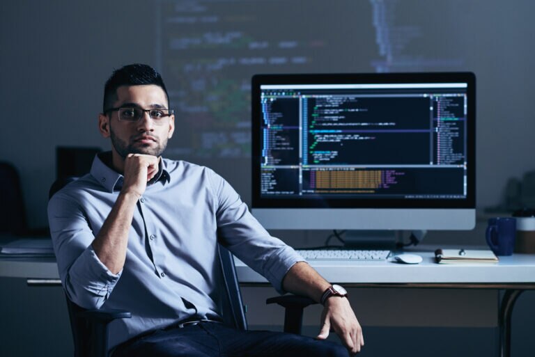 A contemplative programmer sitting in front of a computer displaying code.