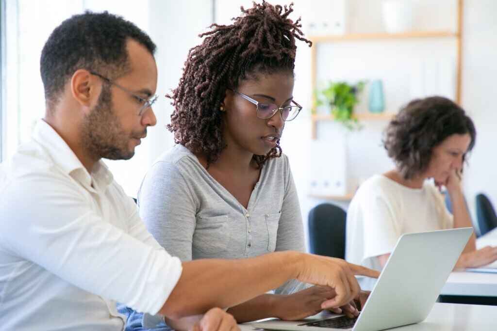 A group of three professionals engaged in a collaborative work session. Two individuals are focused on a laptop