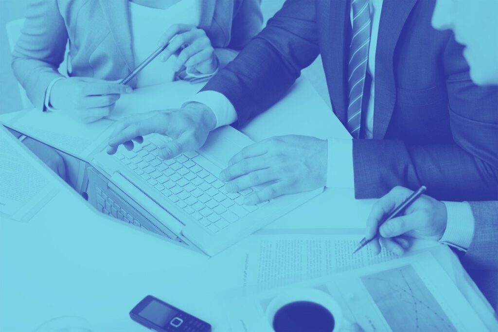 Close-up of hands collaborating over a laptop and documents in a business meeting.