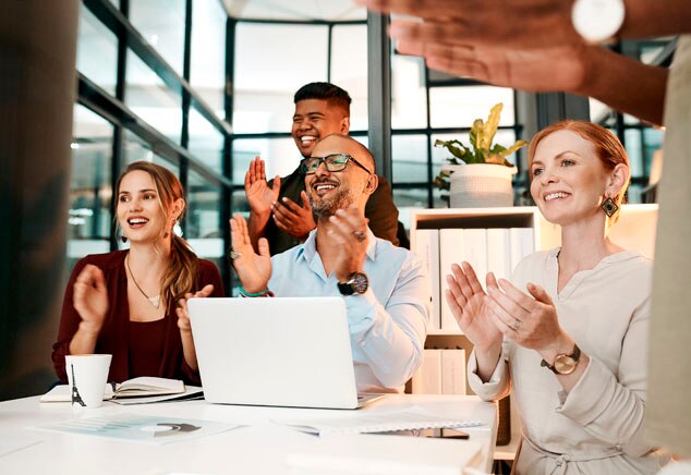 A diverse group of professionals clapping and smiling in an office setting.