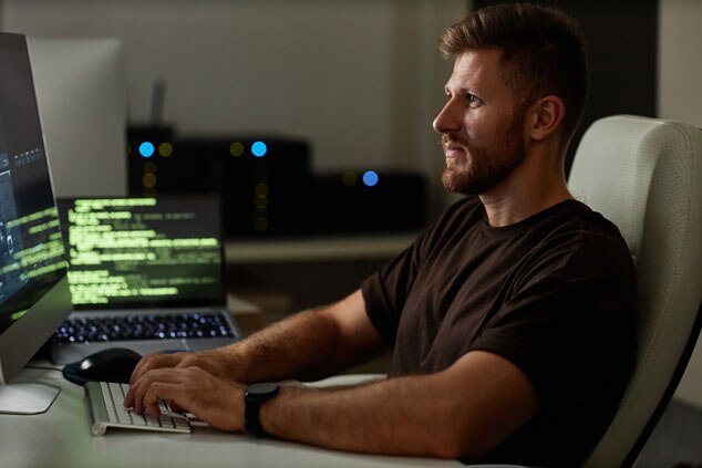 A man coding intently at a computer in a dimly lit workspace