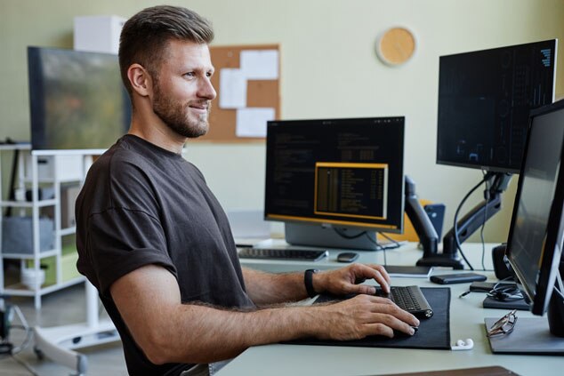 A man sitting at a desk working on a computer,smiling while looking at the screen.