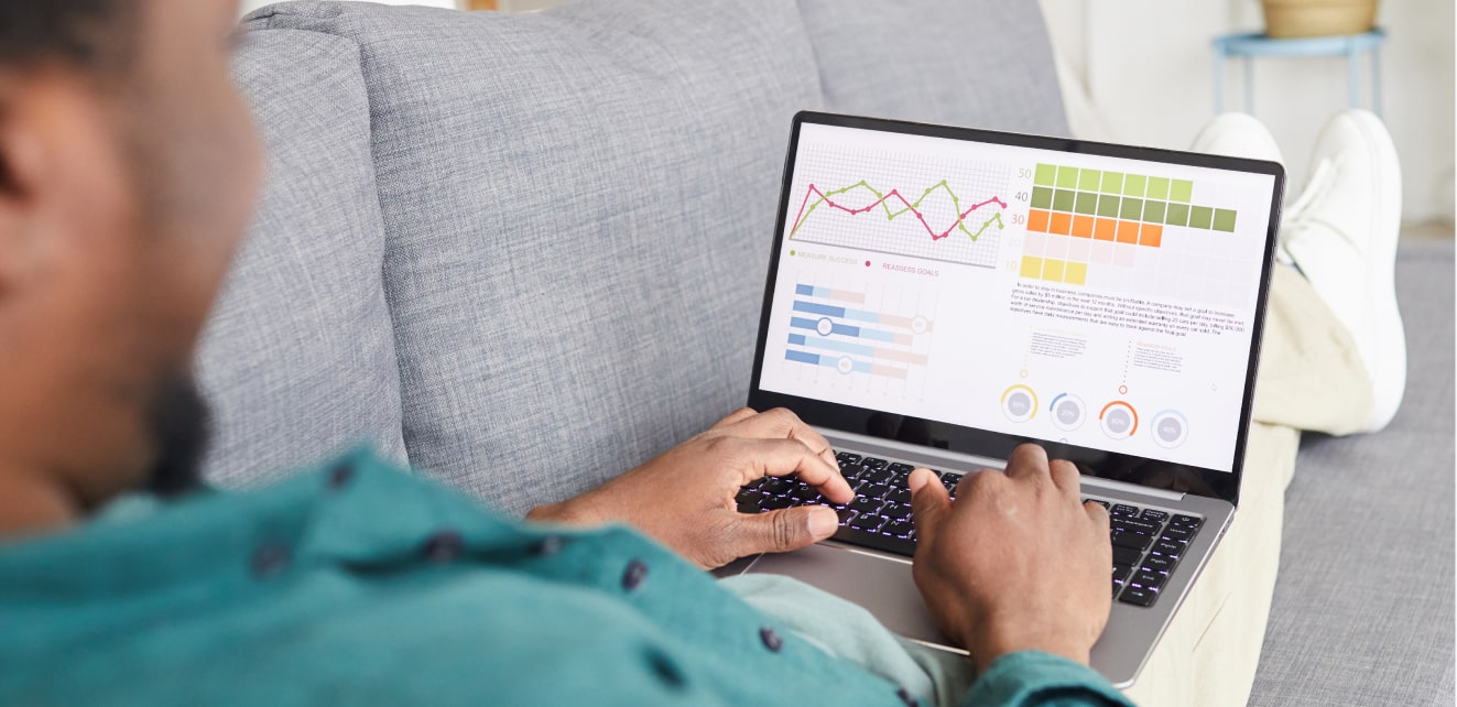 A person sitting on a couch working on a laptop displaying various graphs and data visualizations.