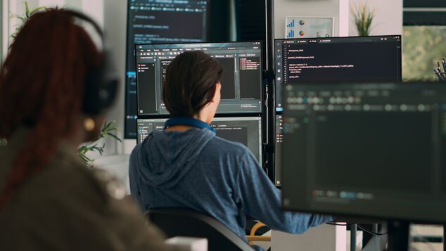 A person sitting at a desk in front of multiple computer monitors displaying code