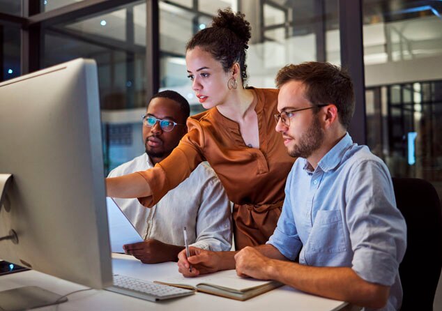 A diverse team collaborating at a computer in a modern office space,focused on a project.