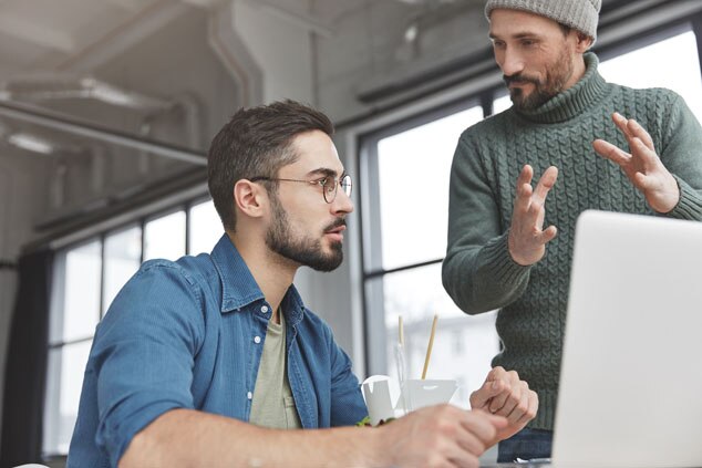 Two men discussing work at a computer in a bright, modern office.