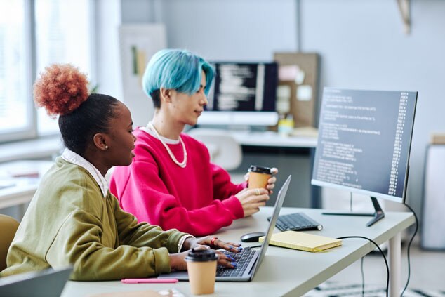 Two individuals coding on laptops with coffee cups in a modern workspace.