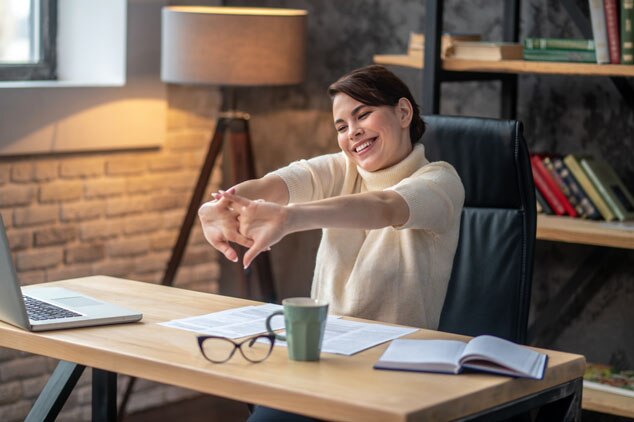 A woman happily stretching at her desk in a cozy workspace