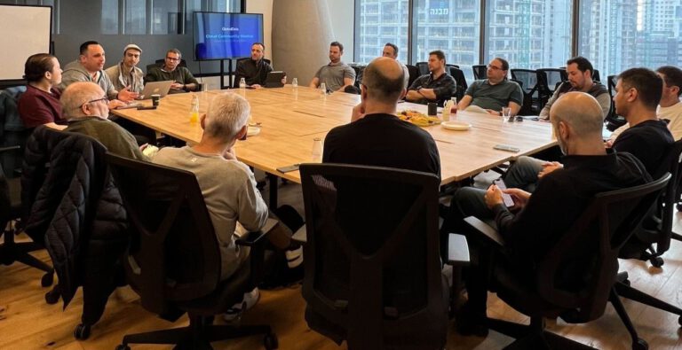 A group of individuals sitting around a large conference table in a modern meeting room,engaged in discussion.