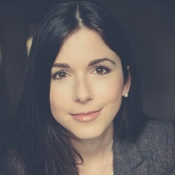 A close-up portrait of a woman with long dark hair,smiling softly,wearing a blazer.