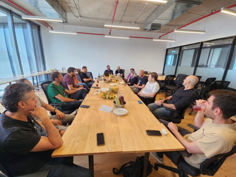 A group of individuals gathered around a long table in a meeting room,discussing and enjoying refreshments.