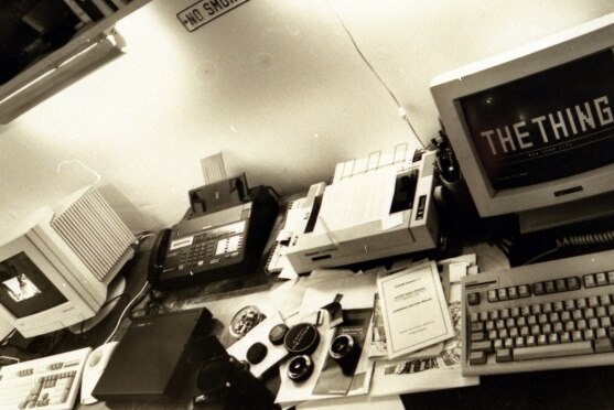 A vintage computer setup with monitors, papers, and various tech equipment.