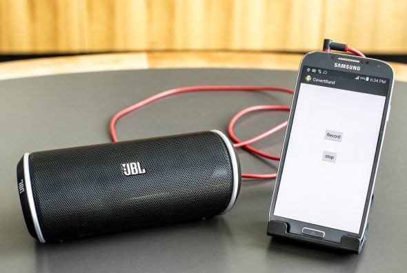 A JBL portable speaker next to a Samsung smartphone displaying a simple app interface with 'Record' and 'Stop' buttons.