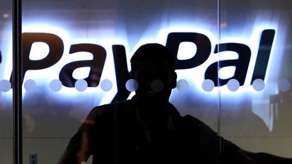 A silhouette of a person in front of a glowing PayPal sign.