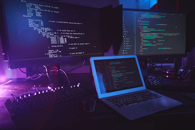 A laptop and dual monitors displaying code with moody lighting.