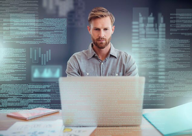 A man focused on his laptop with data and graphs displayed in the background.