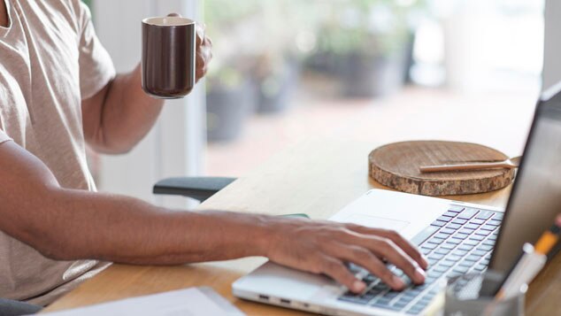 A person holding a coffee mug while typing on a laptop